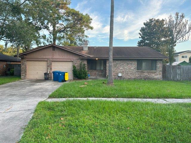 Brick investment home in Jacksonville with attached two car garage and green yard with driveway showing bins outside.